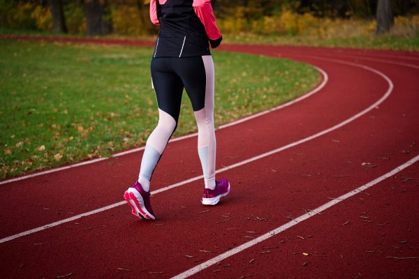 Woman running at track. Female runner jogging at stadium. Active sport exercises at autumn day outdoors. Healthy lifestyle